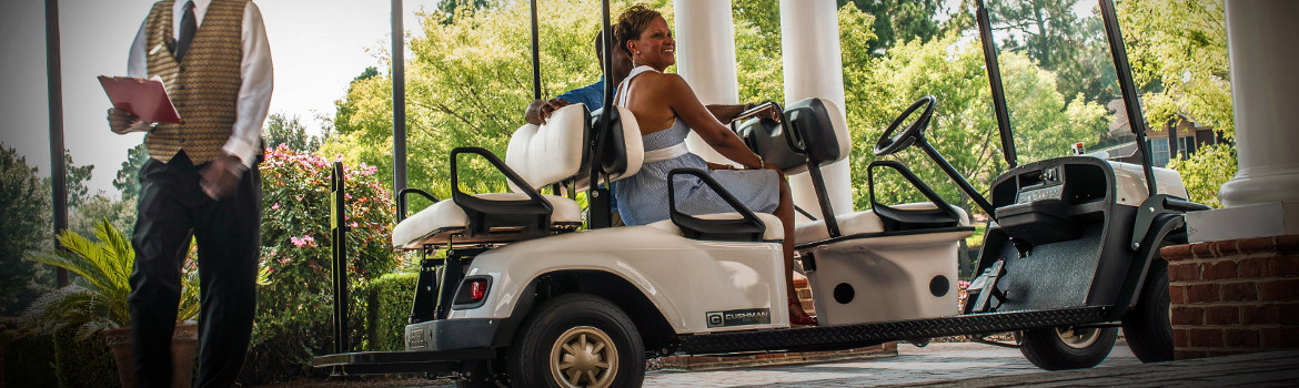 A couple waiting in a Cushman Shuttle 6 golf cart as it's parked outside of a building